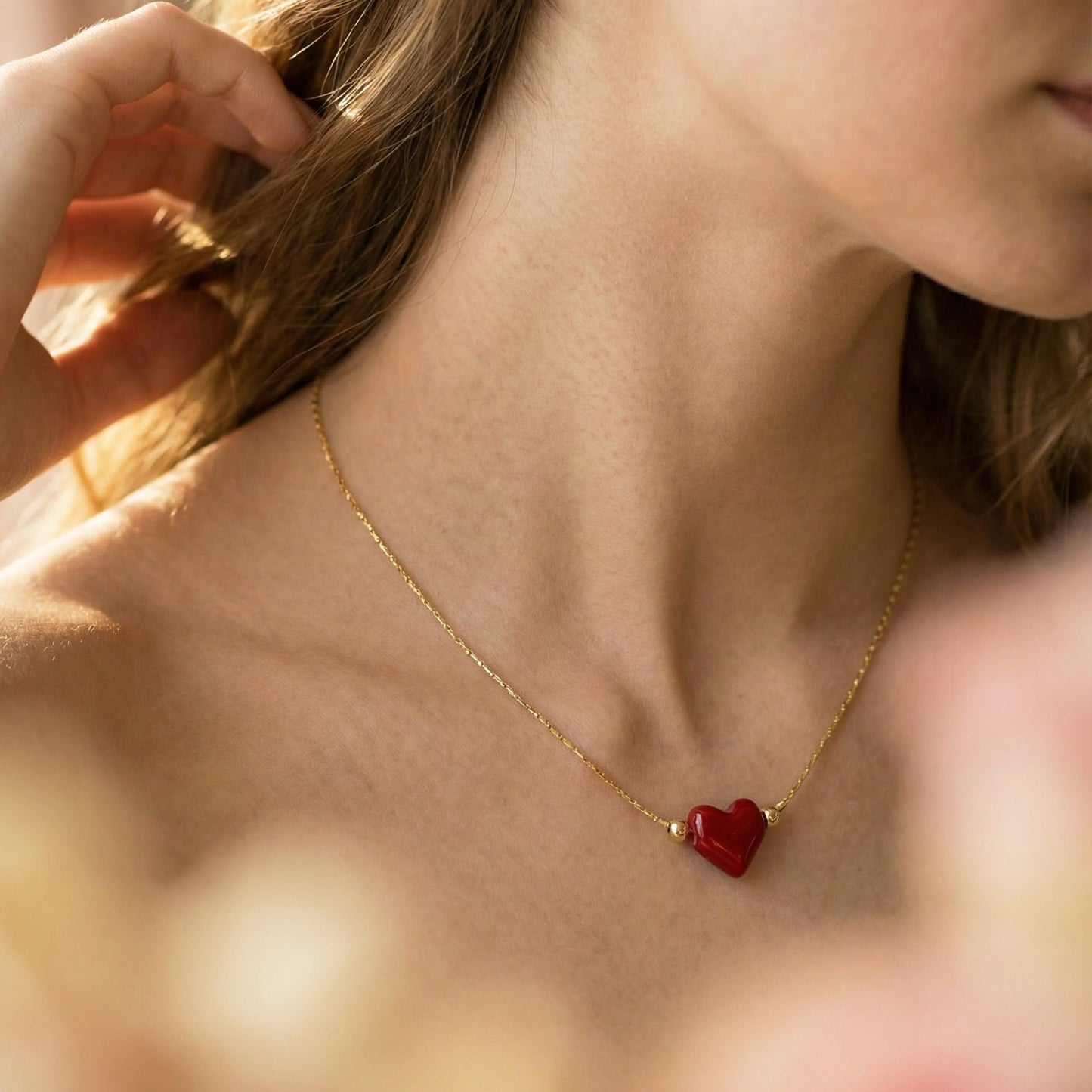 Close-up of a person wearing a gold necklace with a red heart pendant.