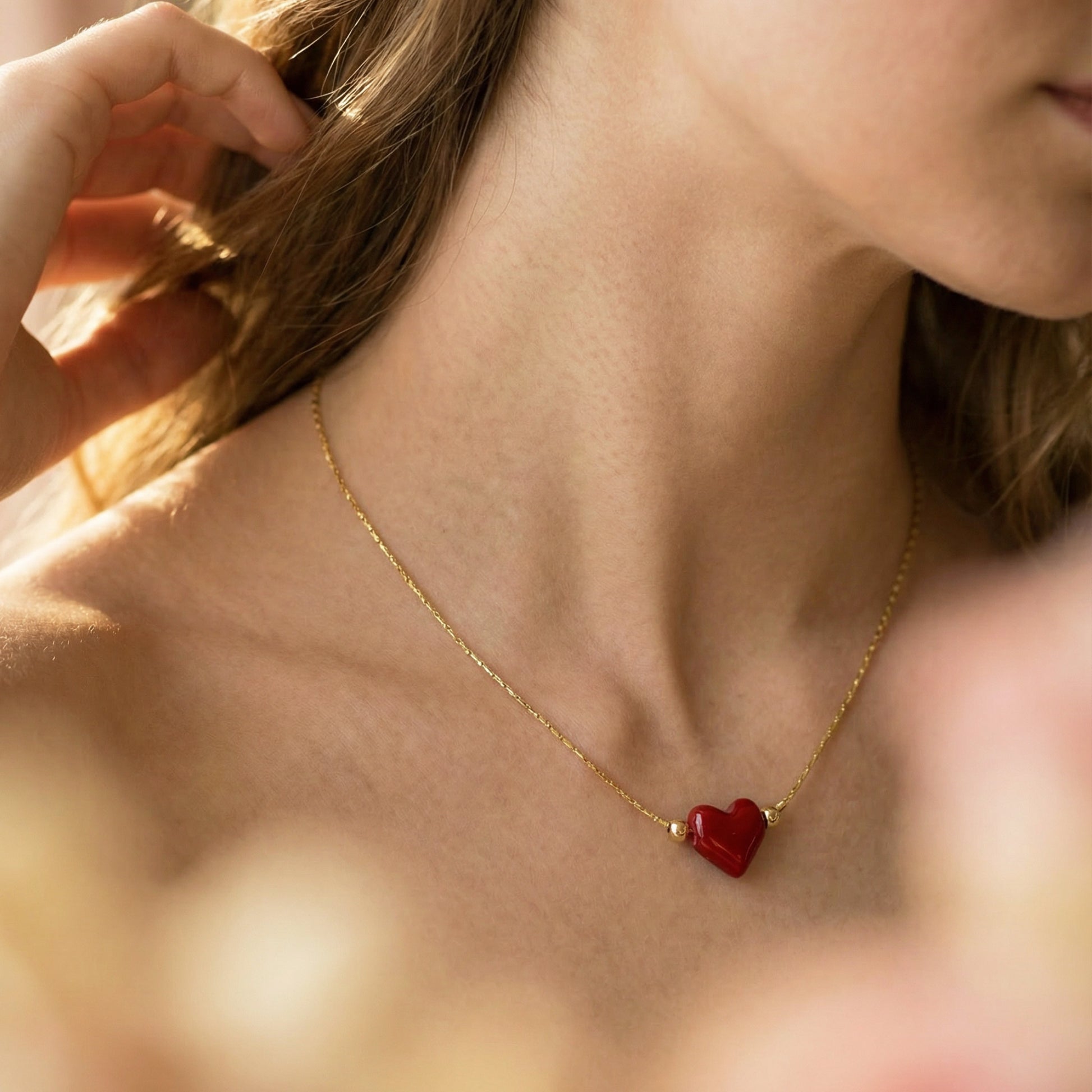 Close-up of a person wearing a gold necklace with a red heart pendant.