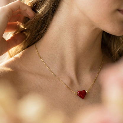 Close-up of a person wearing a gold necklace with a red heart pendant.