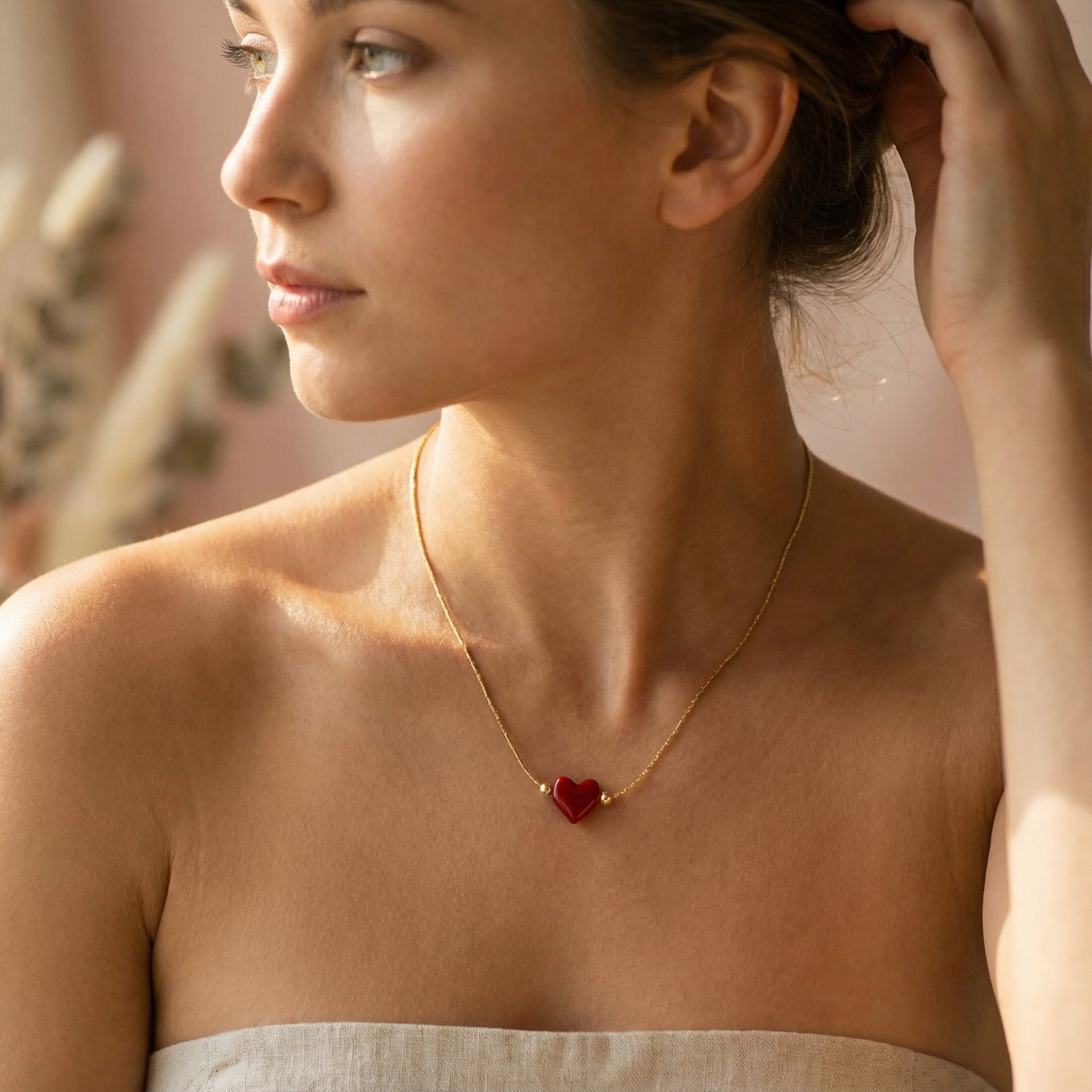 Woman wearing a gold necklace with a red heart pendant.