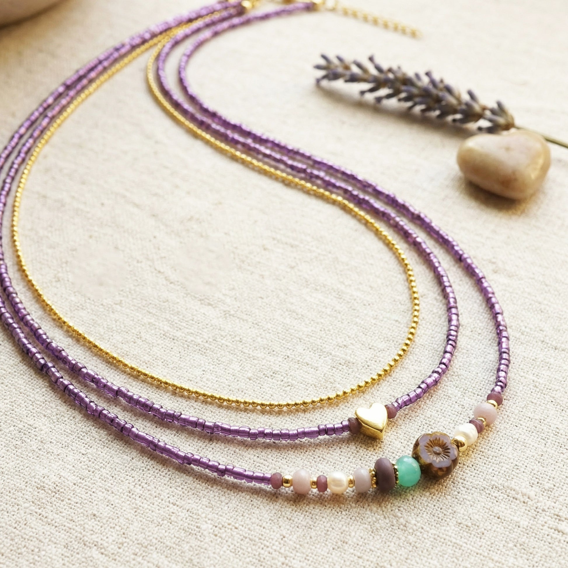 Two beaded necklaces on a textured surface with a stone and lavender sprig.