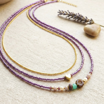 Two beaded necklaces on a textured surface with a stone and lavender sprig.