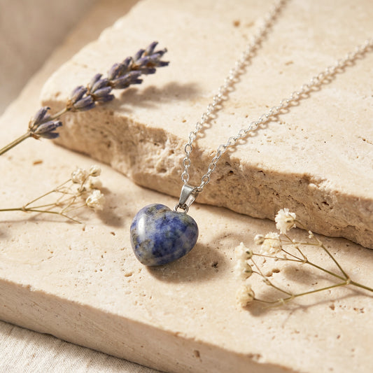 Heart-shaped stone pendant necklace on a beige surface with lavender and dried flowers.