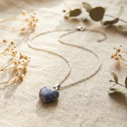 Necklace with a blue stone pendant on a textured fabric background with dried flowers.