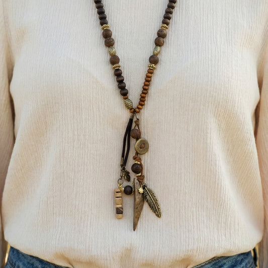 Long beaded necklace with feather and button charms on a beige sweater.