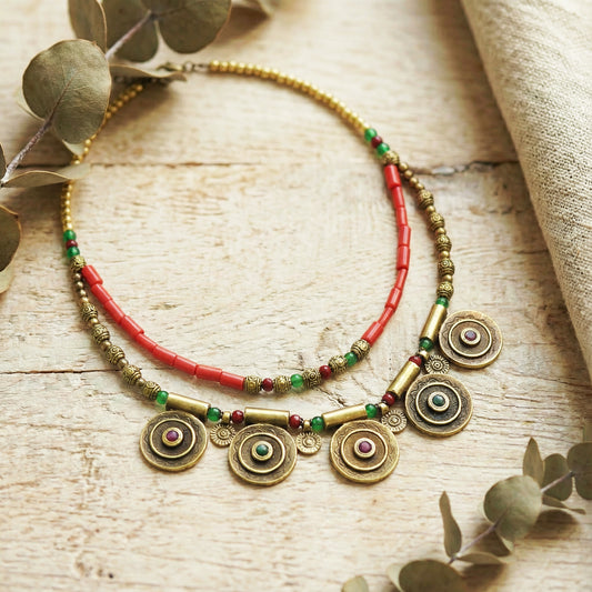 Necklace with gold and red beads on a wooden surface with eucalyptus leaves.