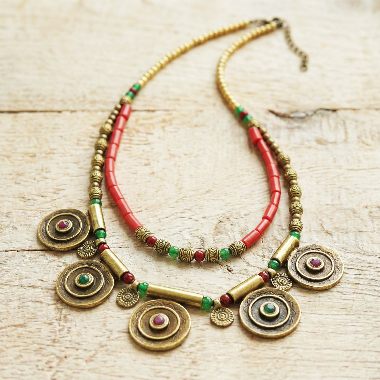 Decorative necklace with red beads and gold circular pendants on a light wooden surface