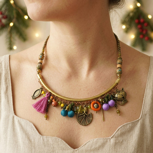 A close-up of a woman wearing a bohemian-style statement necklace. The necklace features a curved gold-tone bar, multi-colored beads, a pink tassel, and various charms including a small owl, a fan, and a miniature cart.