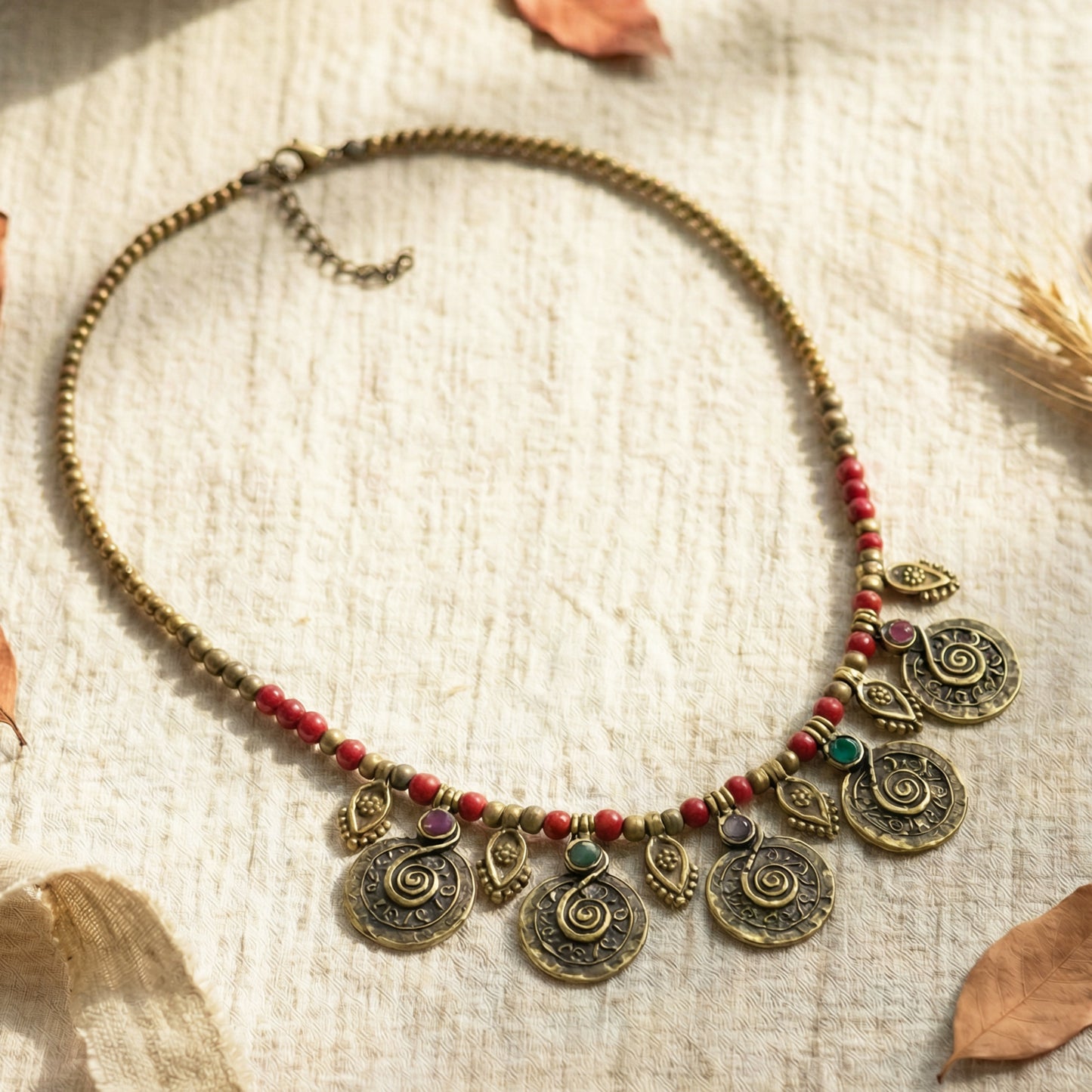Decorative necklace with spiral designs and red beads on a textured fabric background