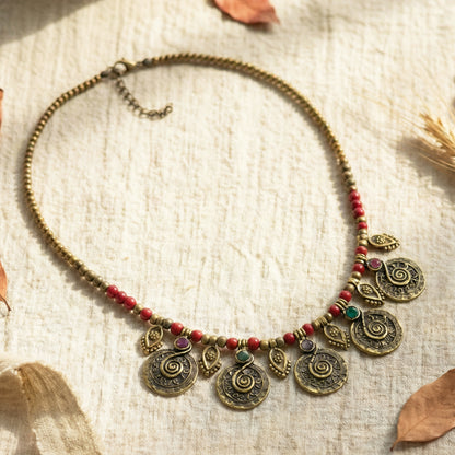 Decorative necklace with spiral designs and red beads on a textured fabric background