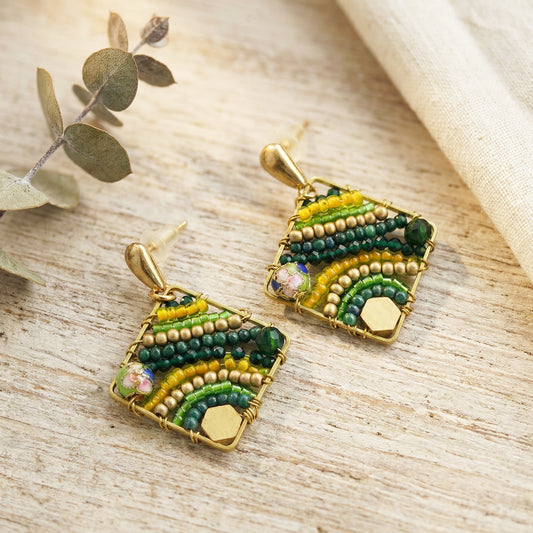 Pair of geometric earrings with green and gold design on a wooden surface.