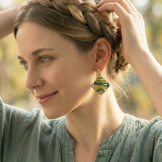 Woman with braided hair wearing green and gold earrings, outdoors.