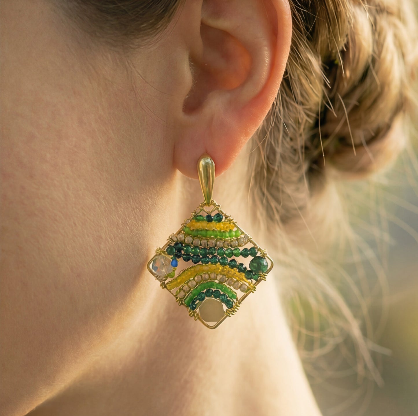 Close-up of a diamond-shaped earring with green and gold details on an ear.