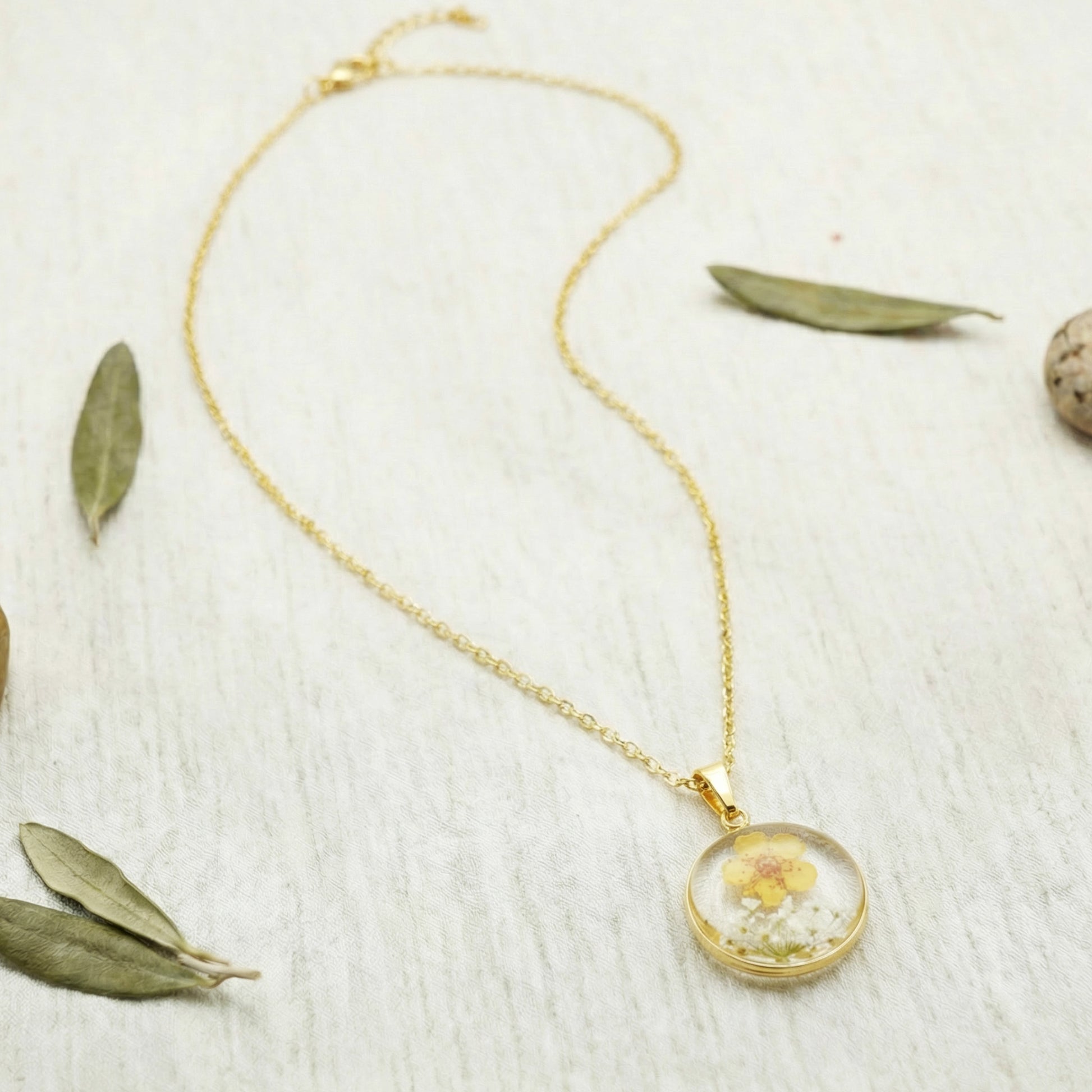 Gold necklace with a round pendant featuring a dried flower on a light wooden surface.
