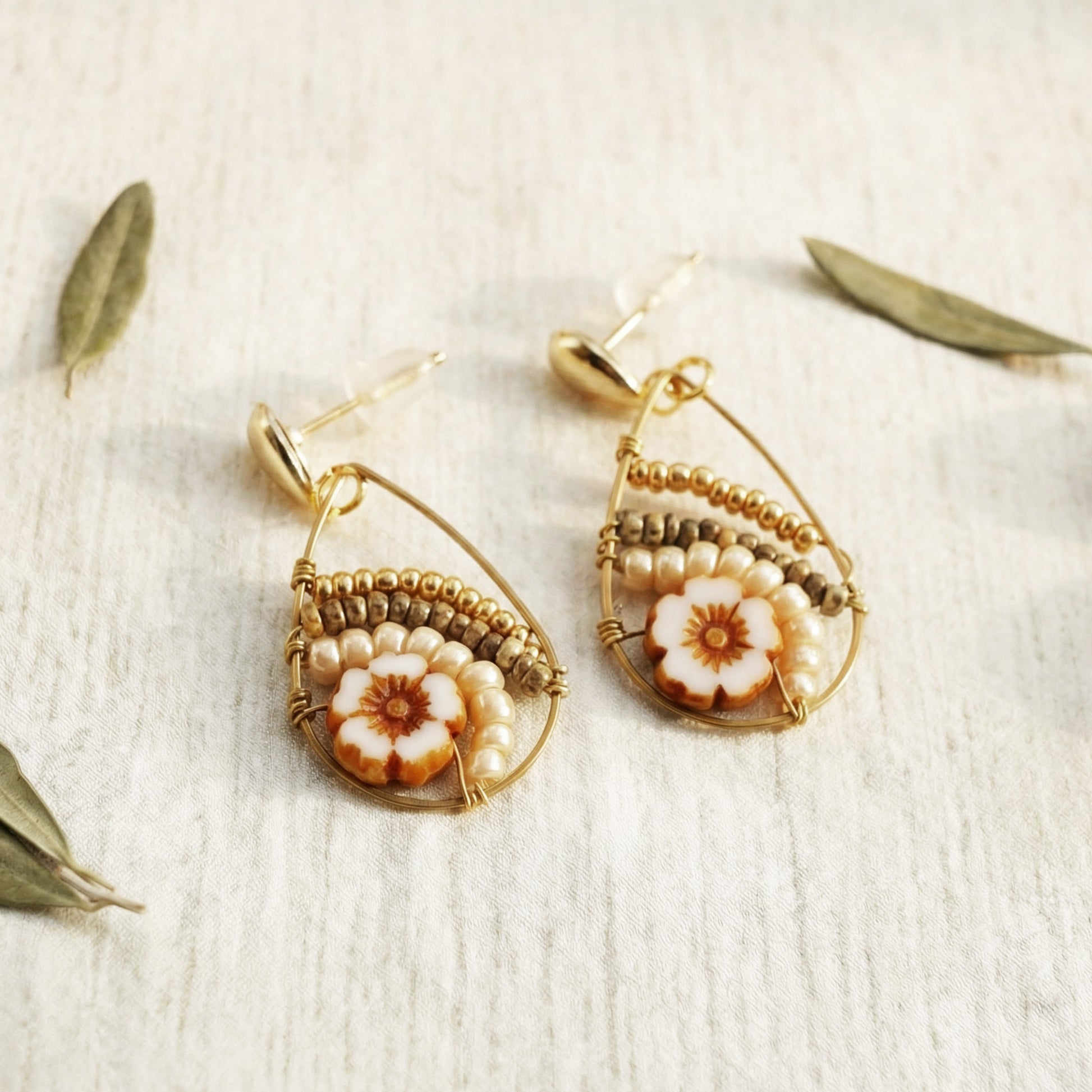Pair of gold earrings with floral designs on a textured beige surface.