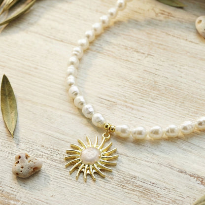 Pearl necklace with a gold sun pendant on a wooden surface