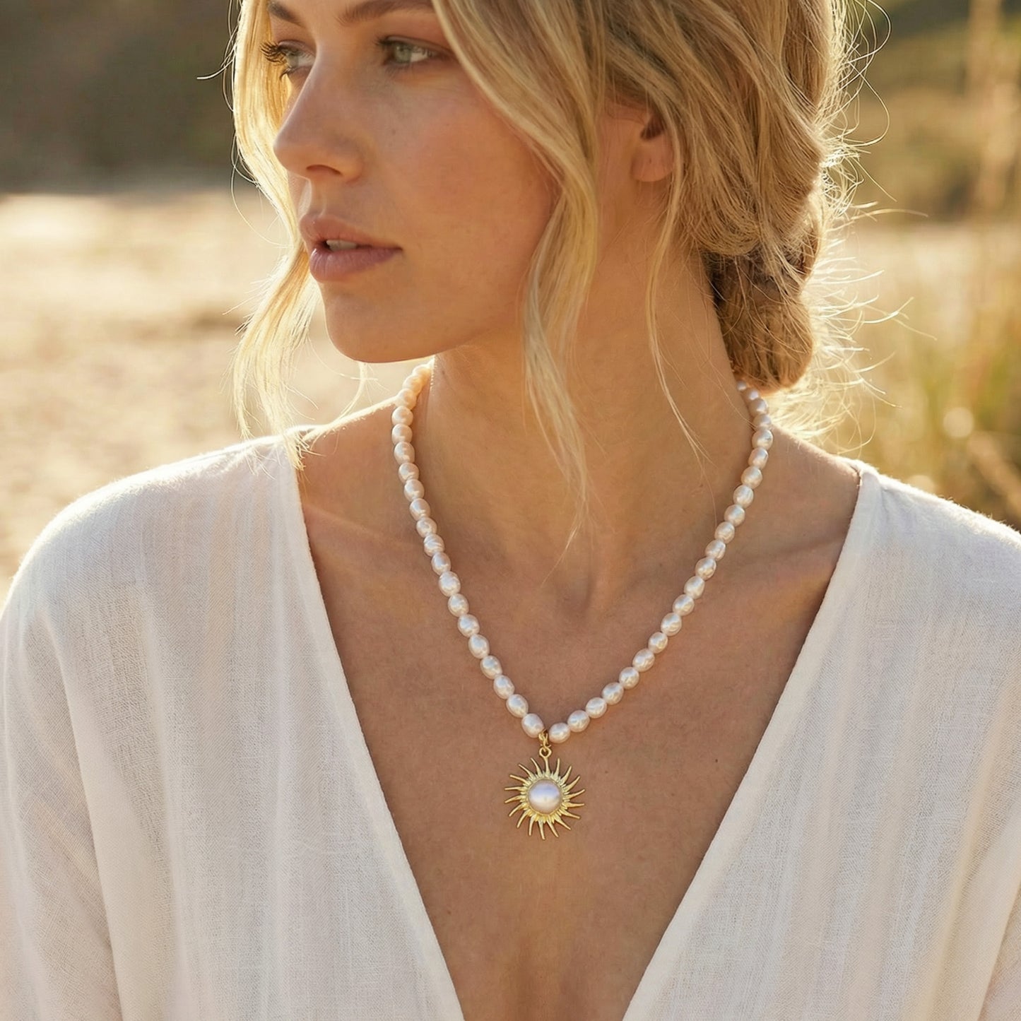 Woman wearing a pearl necklace with a sun pendant in a natural setting