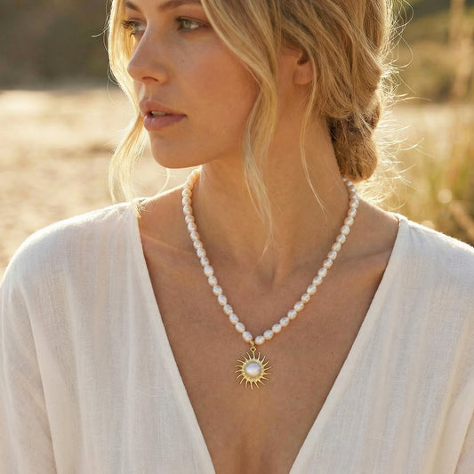 Woman wearing a pearl necklace with a sun pendant in a natural setting