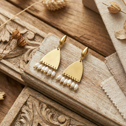 Gold earrings with pearl-like beads on a wooden surface