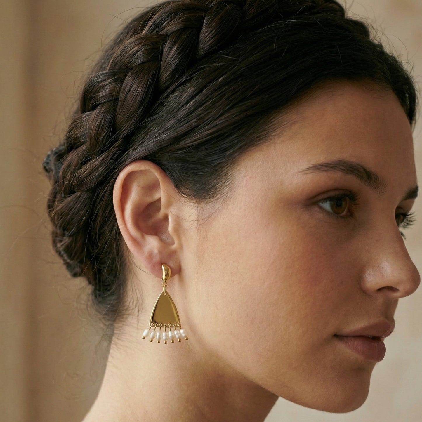 Woman wearing gold earrings with a braided hairstyle against a neutral background