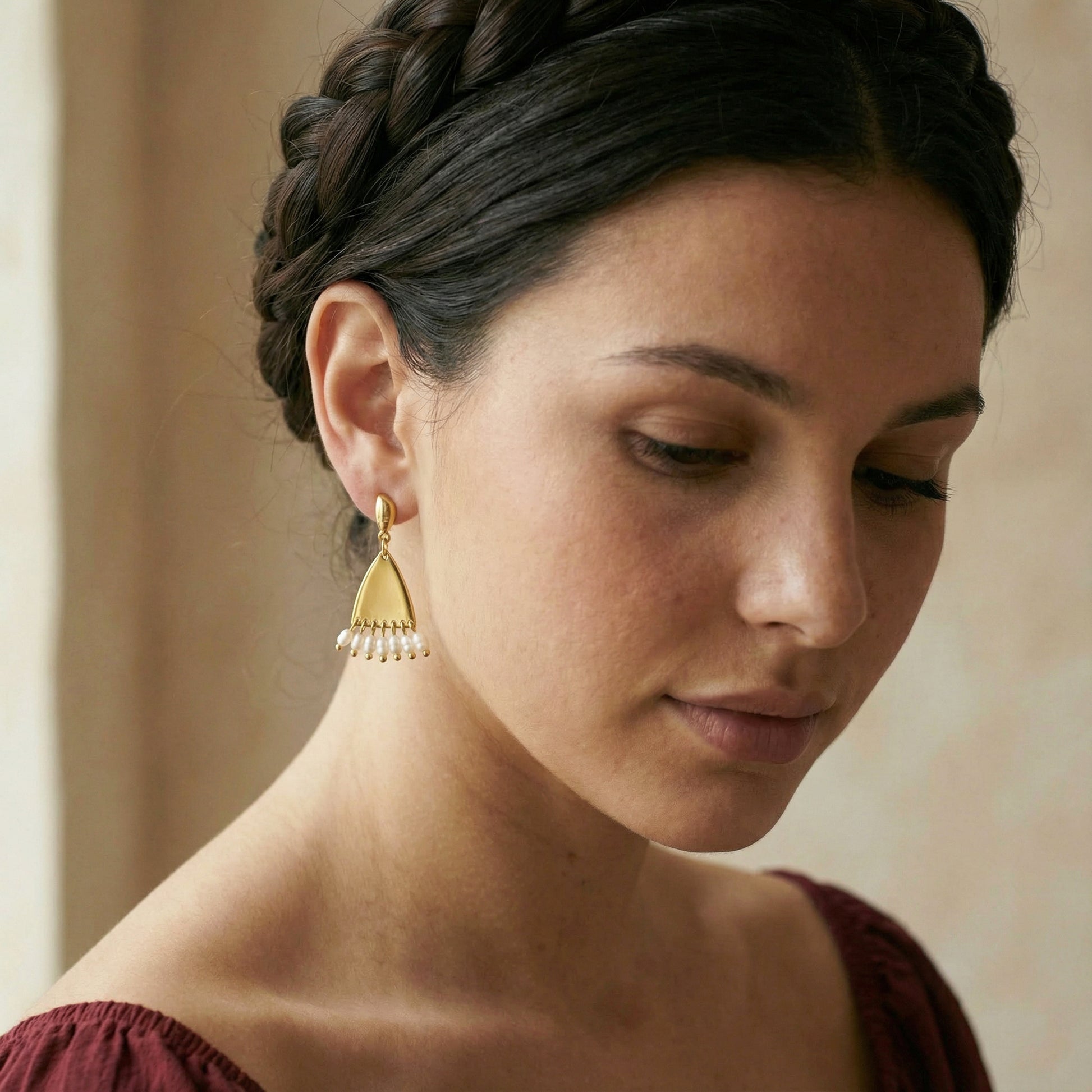 Woman wearing gold triangle earrings with a neutral background