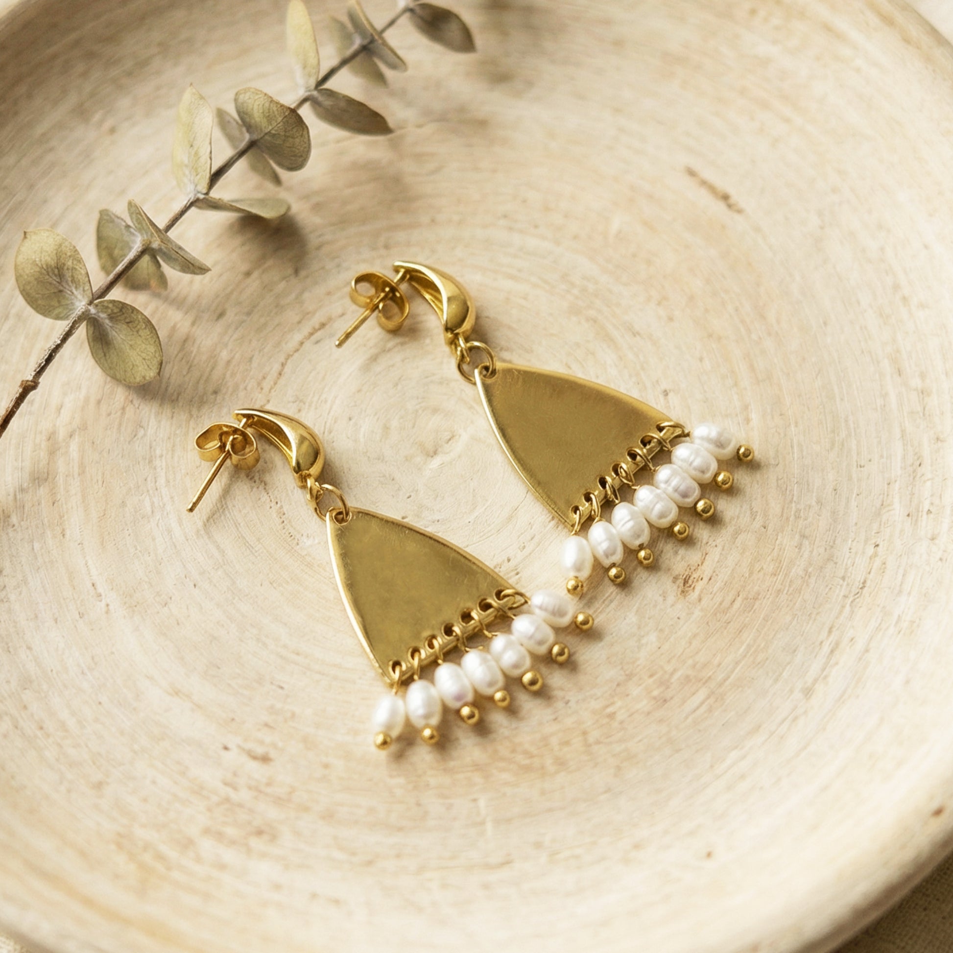 Gold earrings with pearl drops on a wooden surface