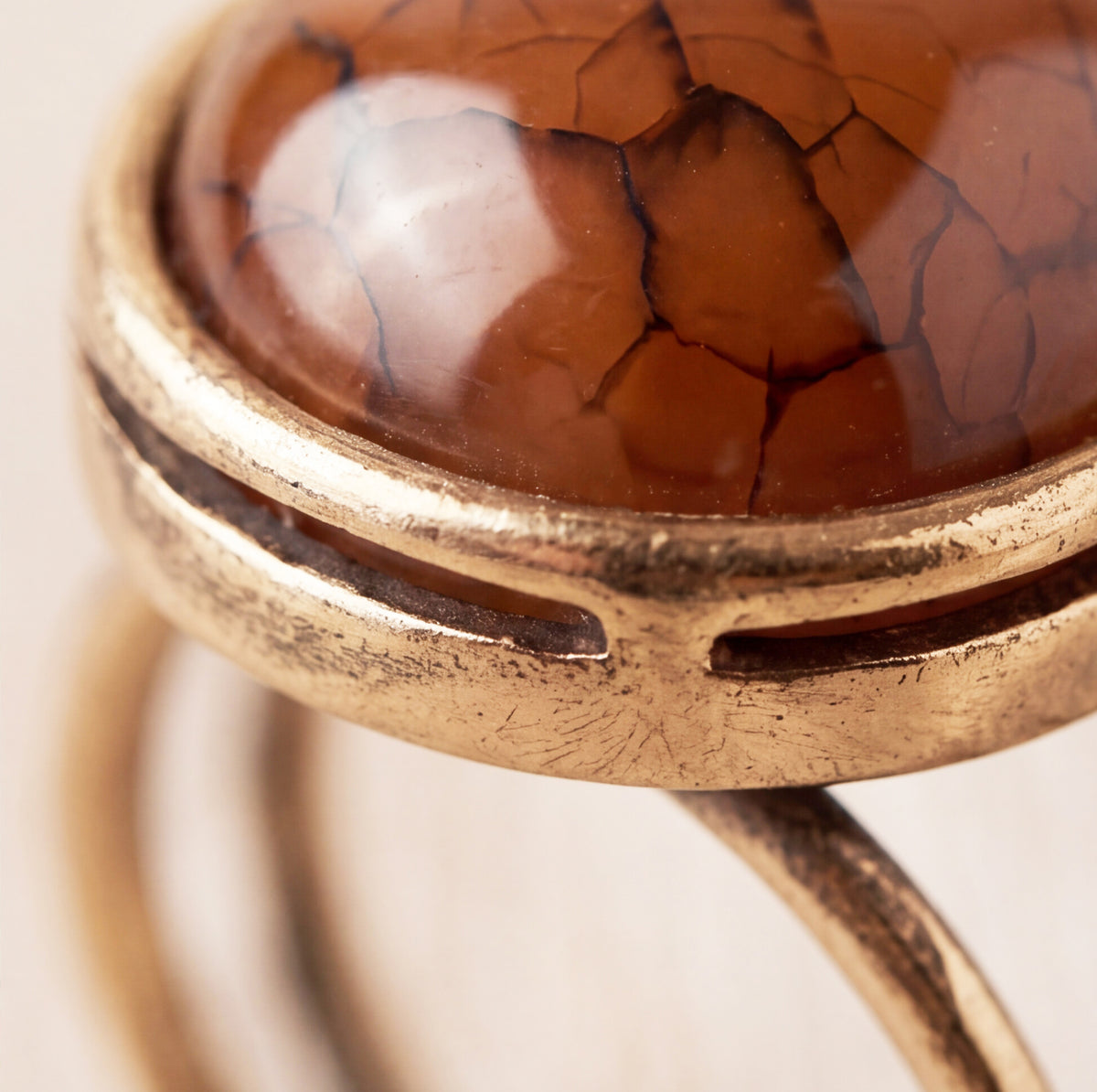 Close-up of a ring featuring a polished oval agate stone with prominent dark crackle veining, set in an antiqued gold-tone metal band.