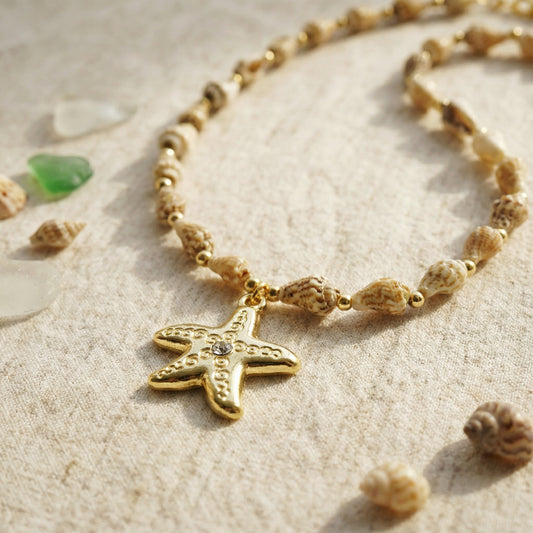 Necklace with starfish pendant on a sandy surface with shells and pebbles.