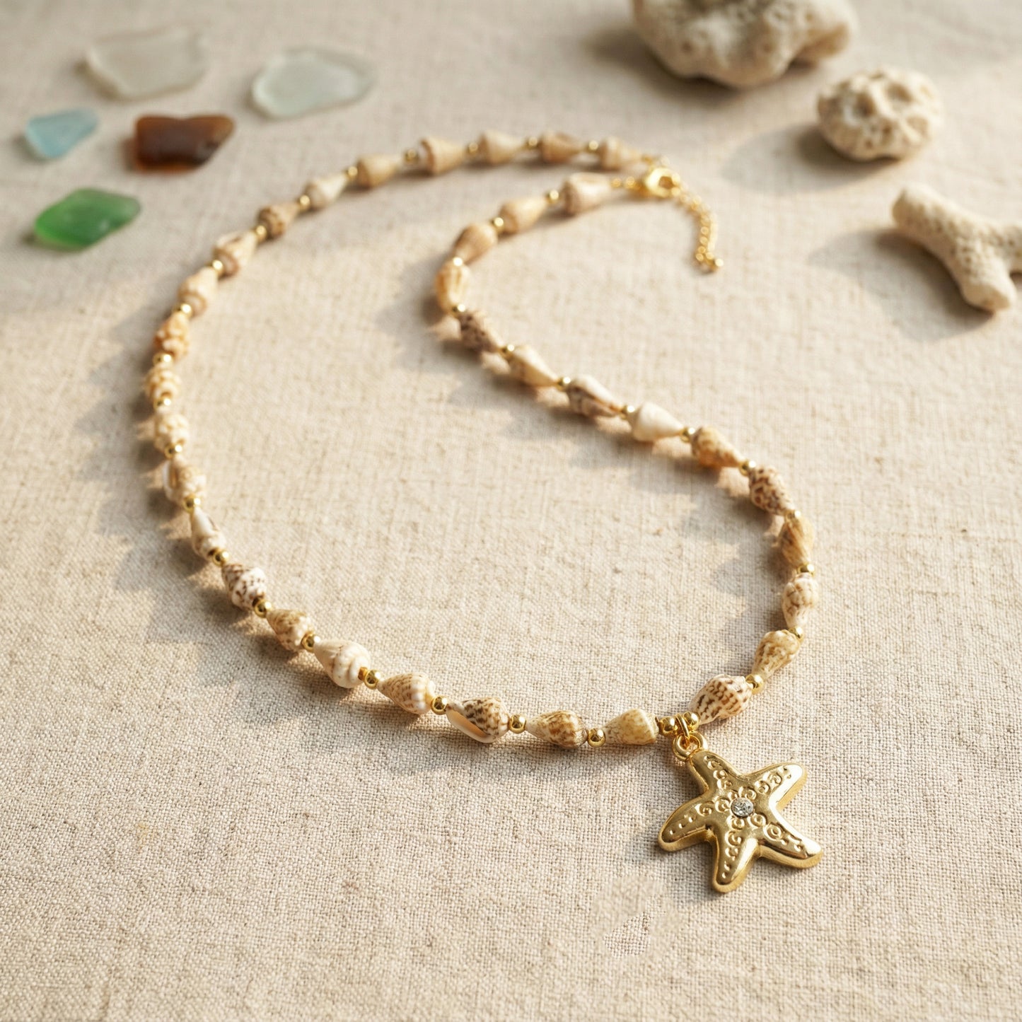 Gold necklace with a starfish pendant on a textured beige surface with seashells.