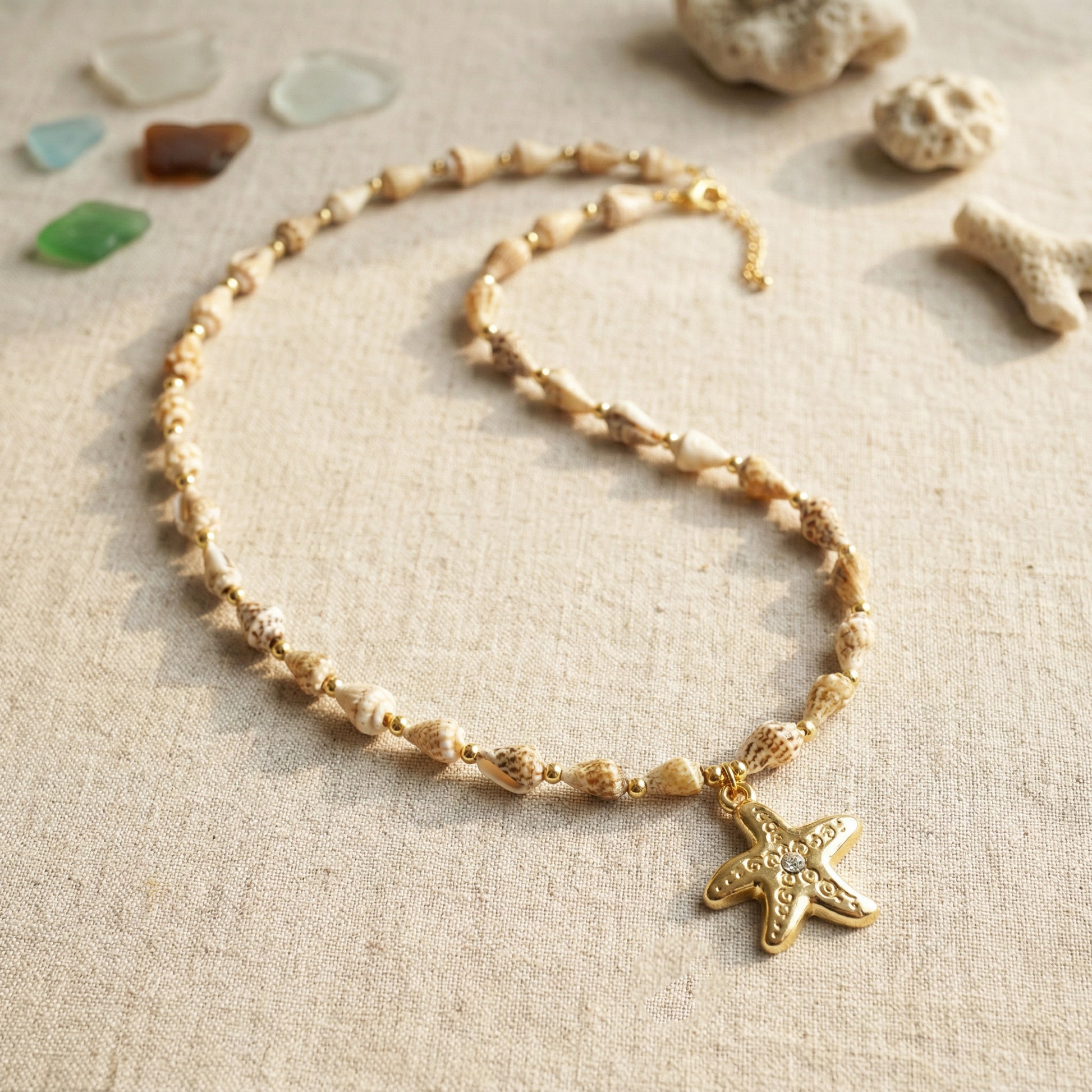 Gold necklace with a starfish pendant on a textured beige surface with seashells.