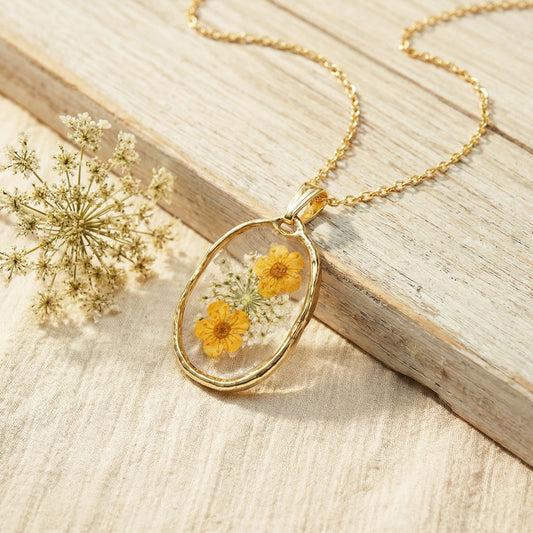 Gold necklace with a pendant featuring pressed yellow flowers on a wooden surface.