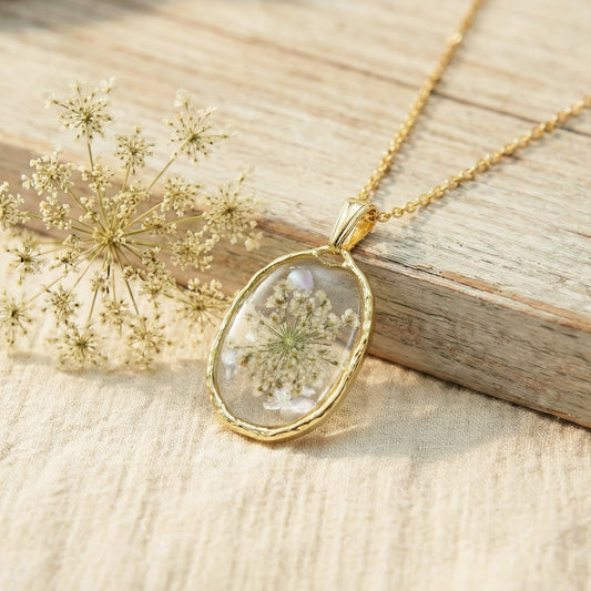 Gold necklace with a pendant featuring a pressed flower on a wooden surface