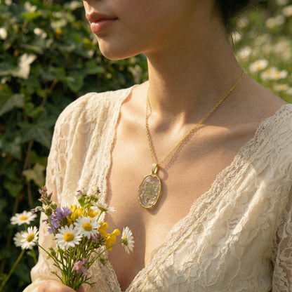 Woman wearing a gold necklace with a pendant, holding flowers in a natural setting