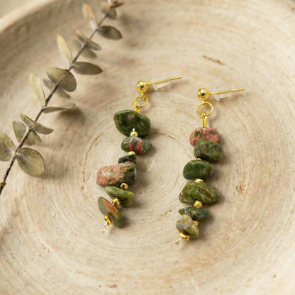 Pair of green stone earrings on a wooden surface with a branch.