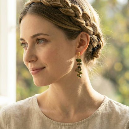 Woman with braided hair and earrings, wearing a light-colored top, outdoors.