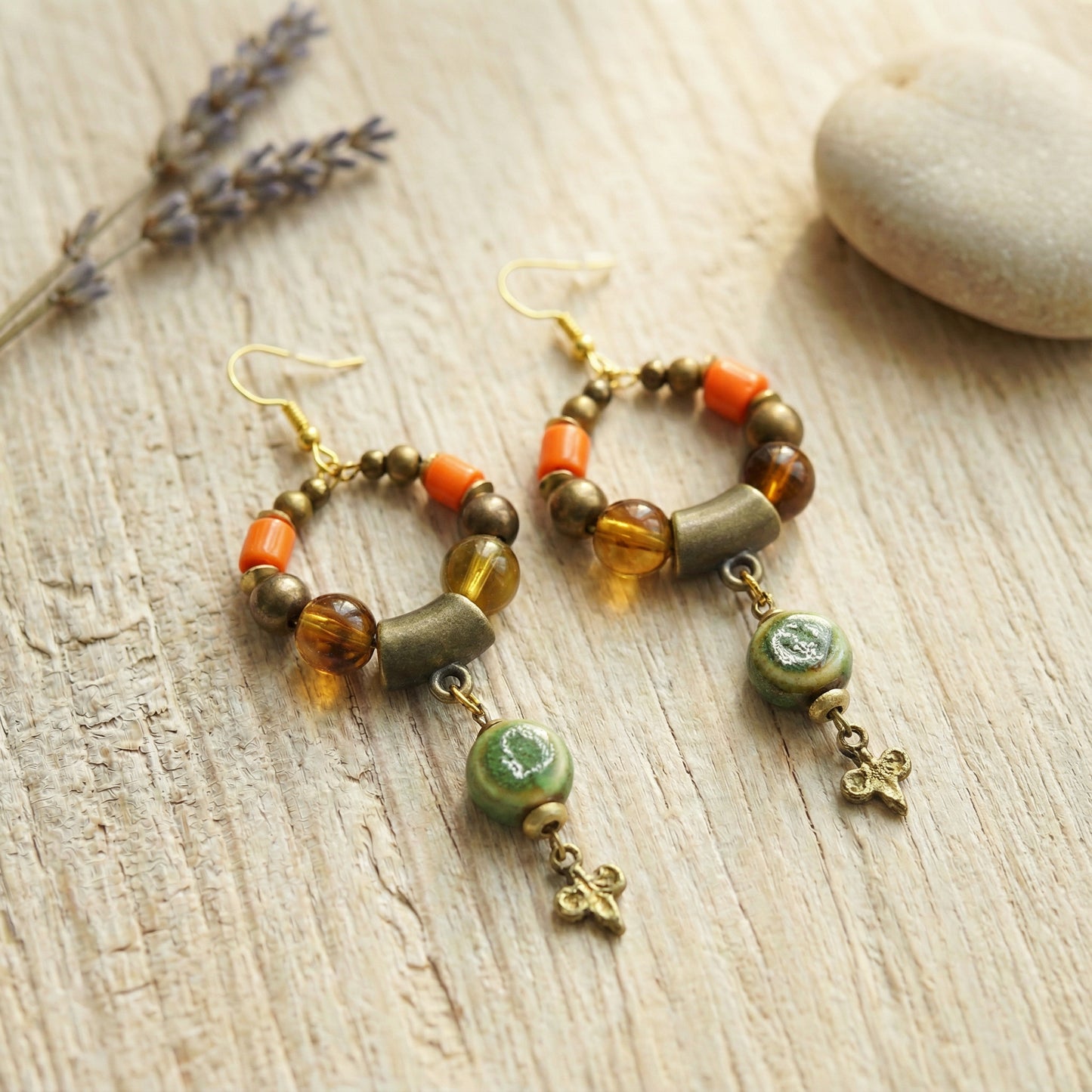 Pair of beaded earrings on a wooden surface with lavender and a stone.