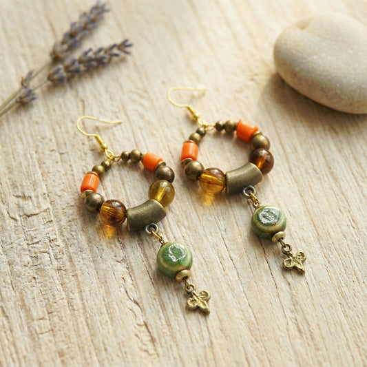 Pair of beaded earrings on a wooden surface with lavender and a stone.