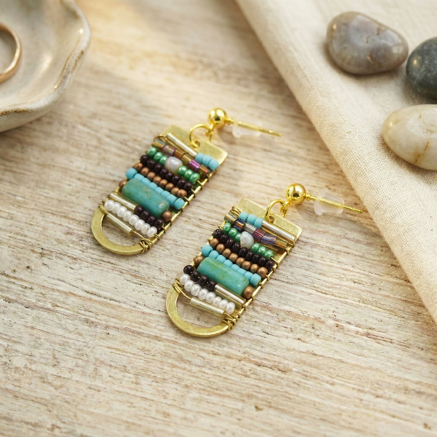 Beaded earrings on a wooden surface with stones in the background