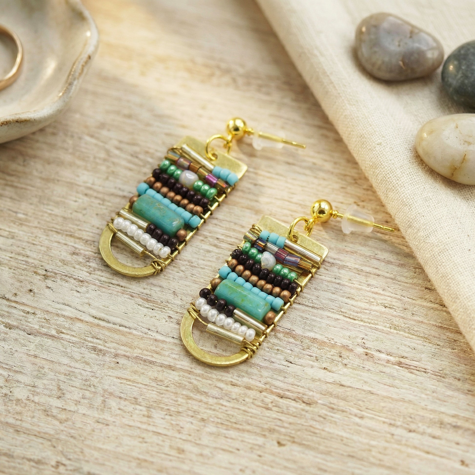 Beaded earrings on a wooden surface with stones in the background