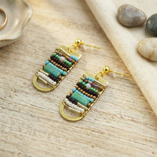 Beaded earrings on a wooden surface with stones in the background