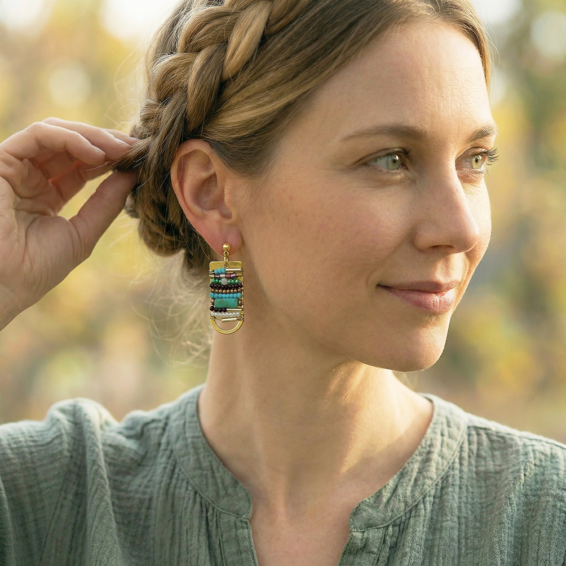 Woman wearing colorful earrings outdoors with blurred natural background