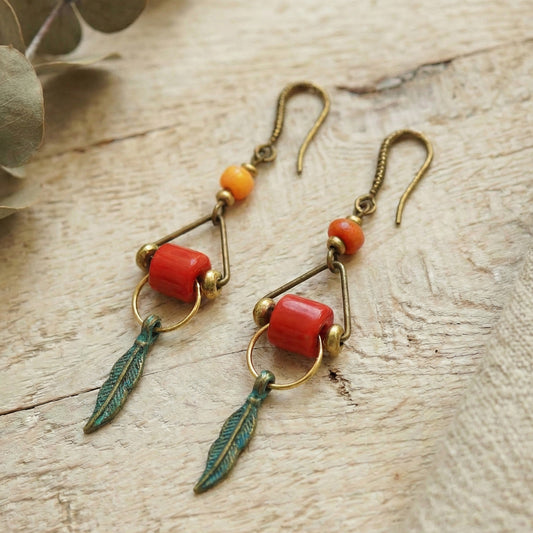 Pair of earrings with red beads and green feather-like charms on a wooden surface.