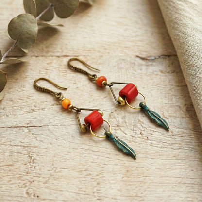 Pair of earrings with red and green beads on a wooden surface