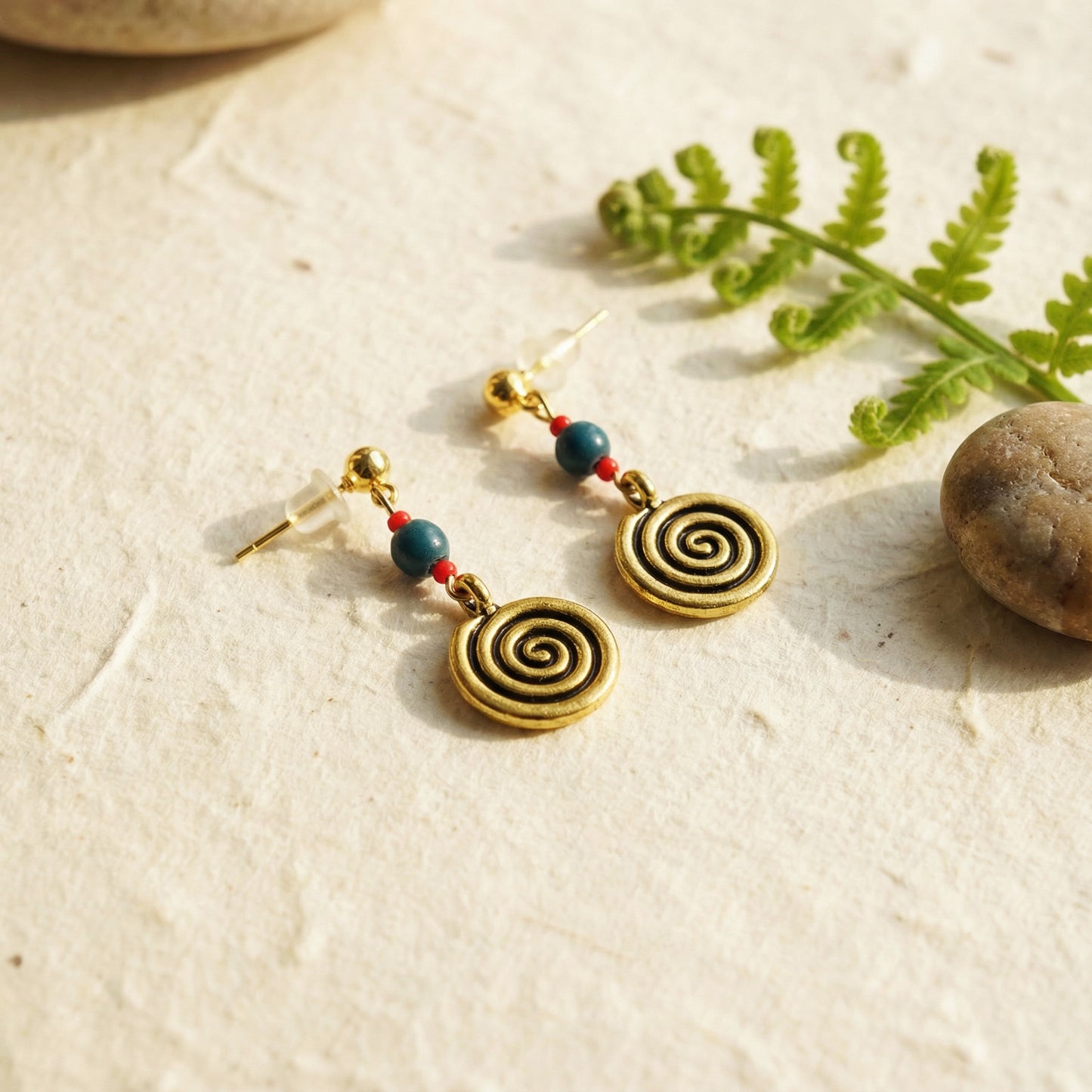 Spiral earrings with beads on a natural stone surface with fern leaves.