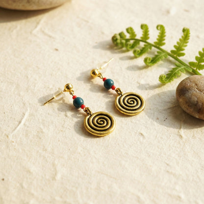 Spiral earrings with beads on a natural stone surface with fern leaves.