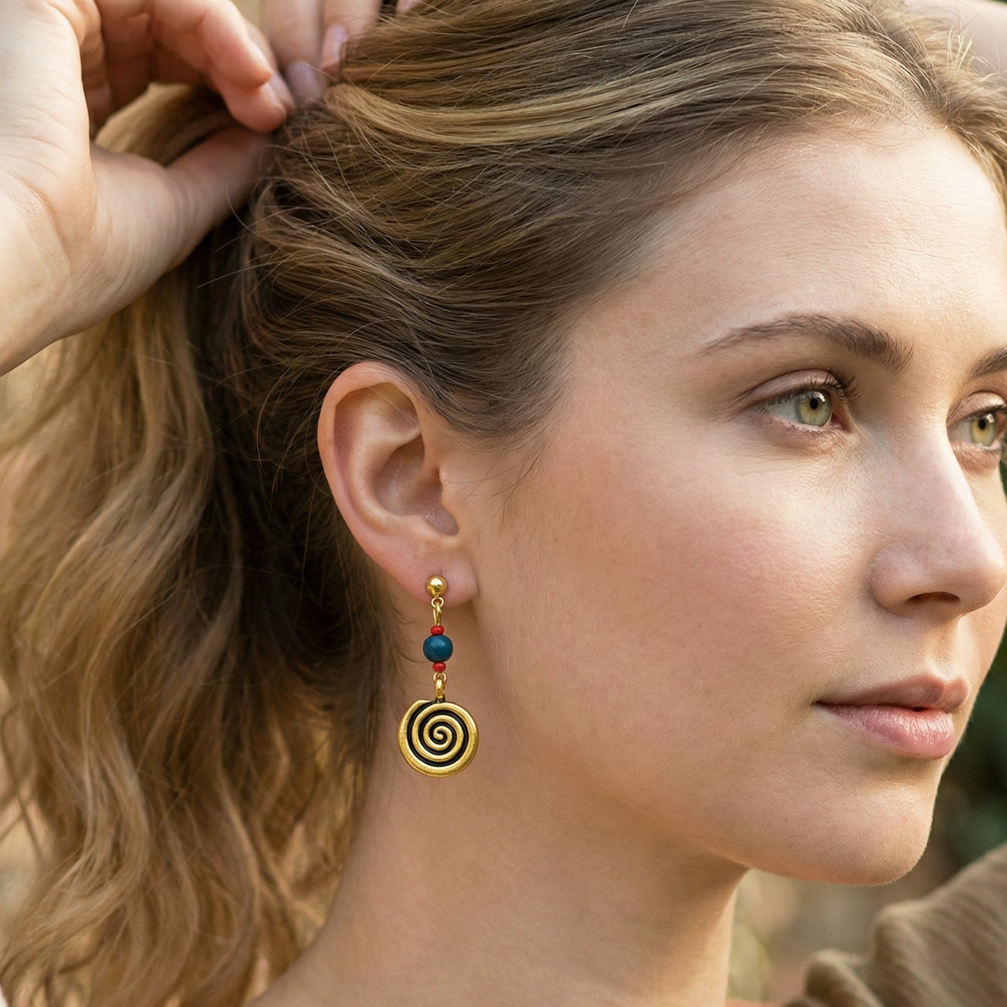 Close-up of a woman wearing spiral earrings with colored stones.