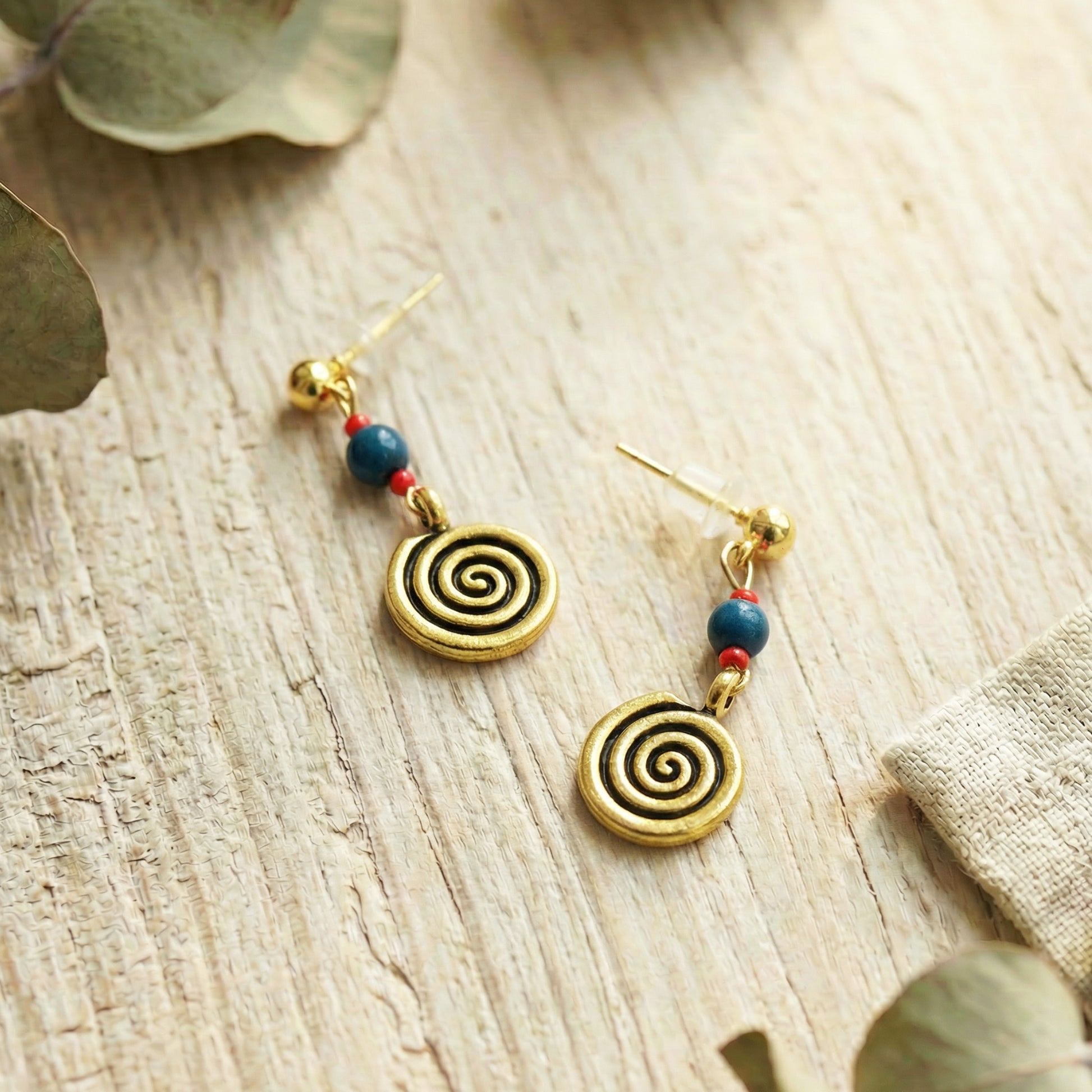Gold spiral earrings with colorful beads on a wooden surface