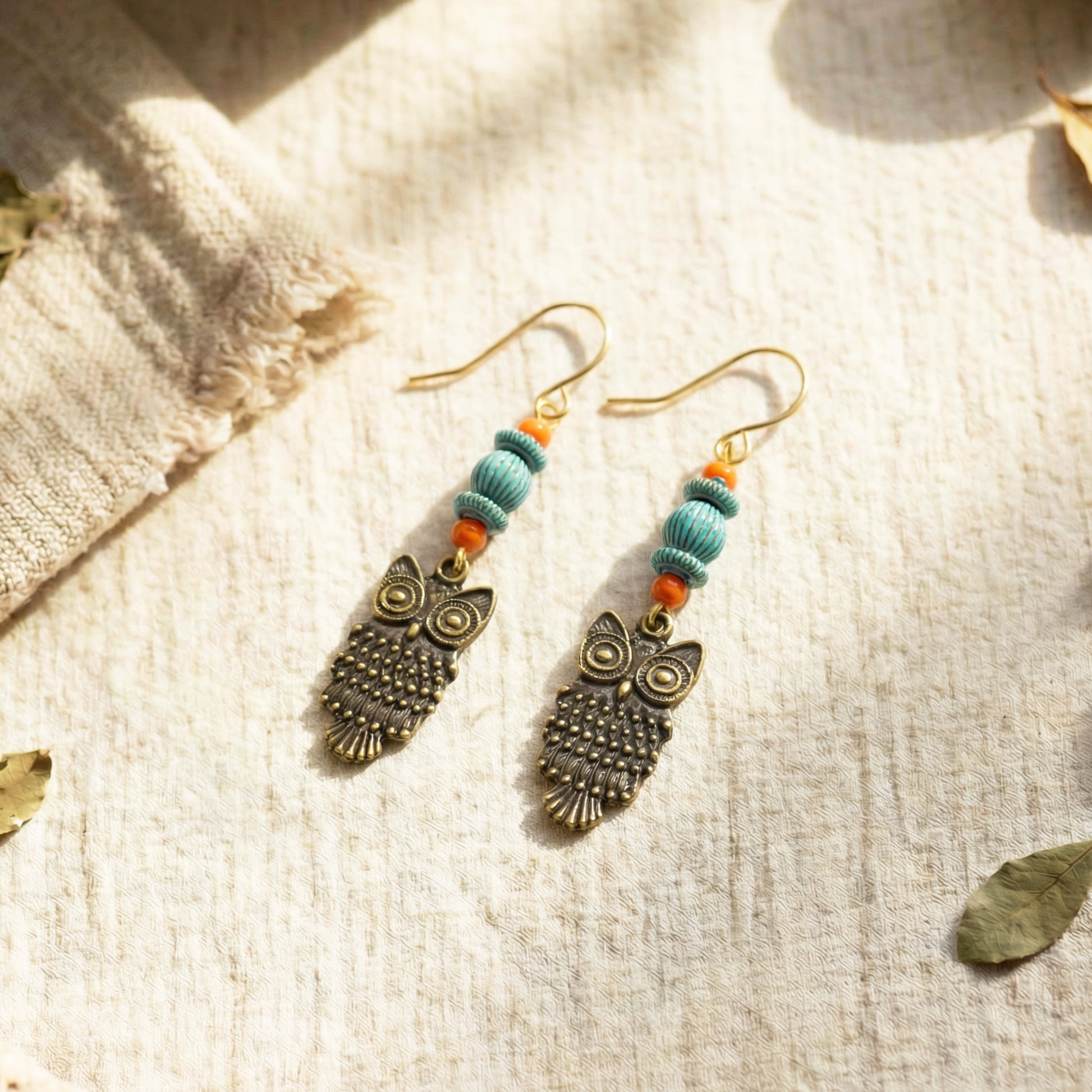 Owl-shaped earrings with turquoise beads on a textured fabric background