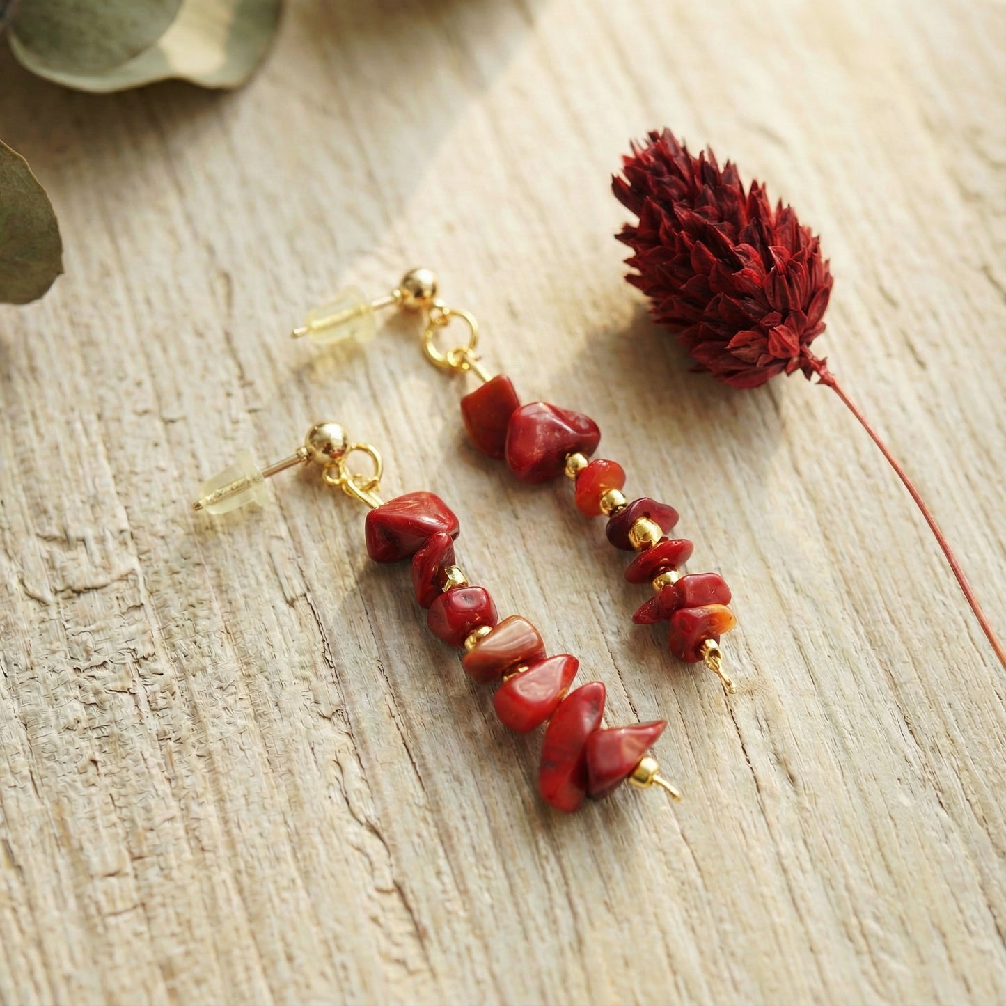 Red stone earrings with gold accents on a wooden surface with a dried flower.